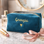 Blue makeup bag with 'Georgia' embroidery on a marble surface with lipsticks and perfume.