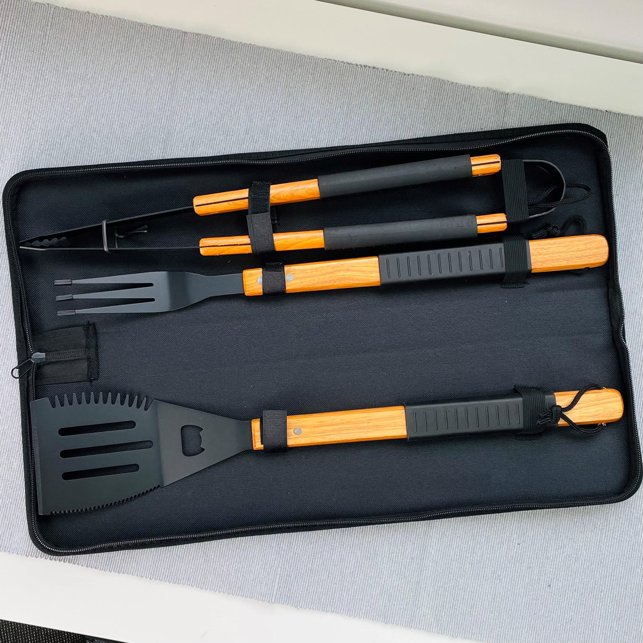 Set of barbecue tools with black and orange handles in a black case on a gray surface.