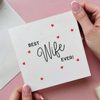 Card with 'Best Wife Ever!' text held by a hand on a pink background