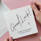 Hand holding a 'Good Luck!' card on a pink background
