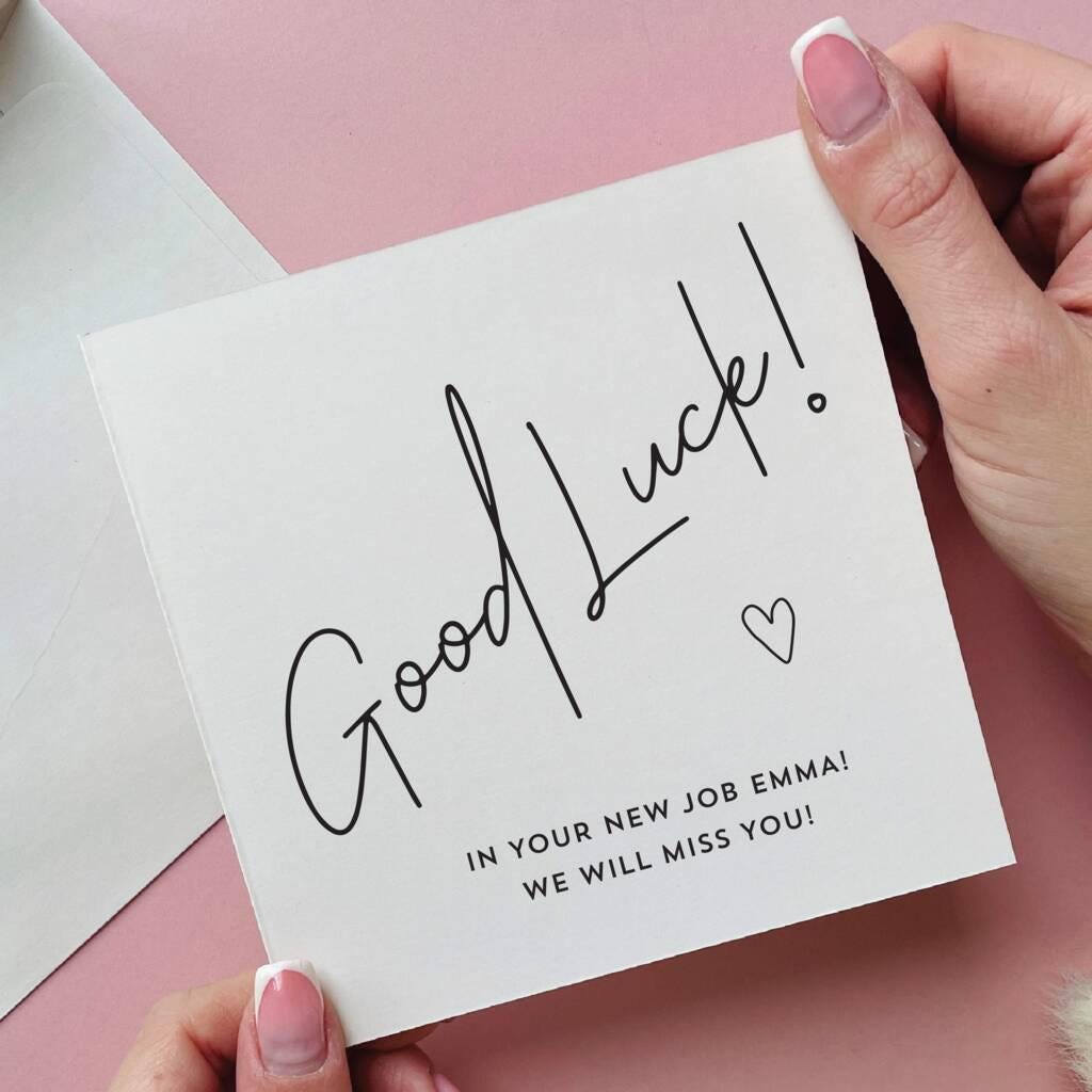 Hand holding a 'Good Luck!' card on a pink background