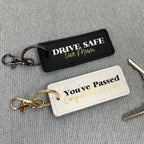 Two keychains on a gray textured background, one with 'Drive Safe' message and the other with 'You've Passed' message.