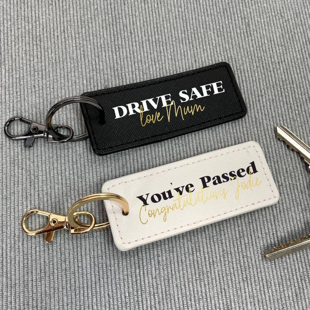 Two keychains on a gray textured background, one with 'Drive Safe' message and the other with 'You've Passed' message.