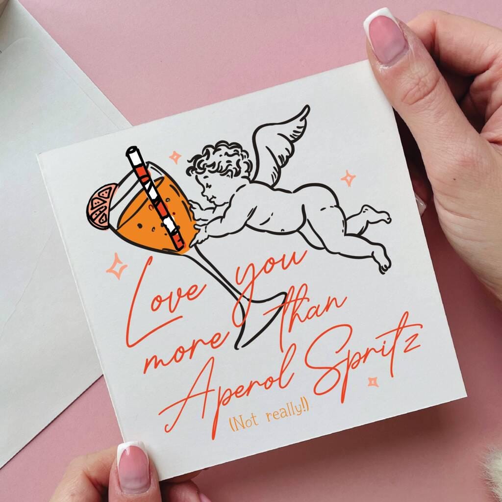 Card with an illustration of a cherub holding a cocktail and text, held by hands on a pink background.