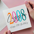Hand holding a birthday card with colorful numbers and 'Happy 18th Birthday' text on a pink background.