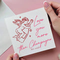 Card with angel illustration and text 'Love you more than Champagne (Not really!)' held by a hand on a pink background