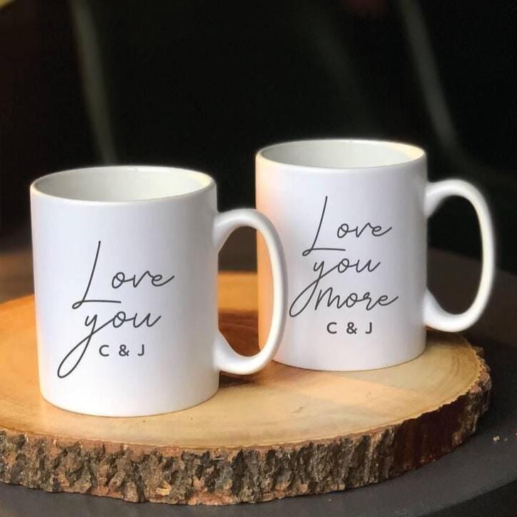 Two white mugs with personalized text on a wooden coaster