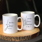 Two white mugs with personalized text on a wooden coaster