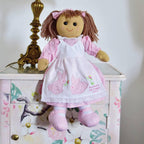 Doll in a pink dress with bunny designs on a decorative cabinet.