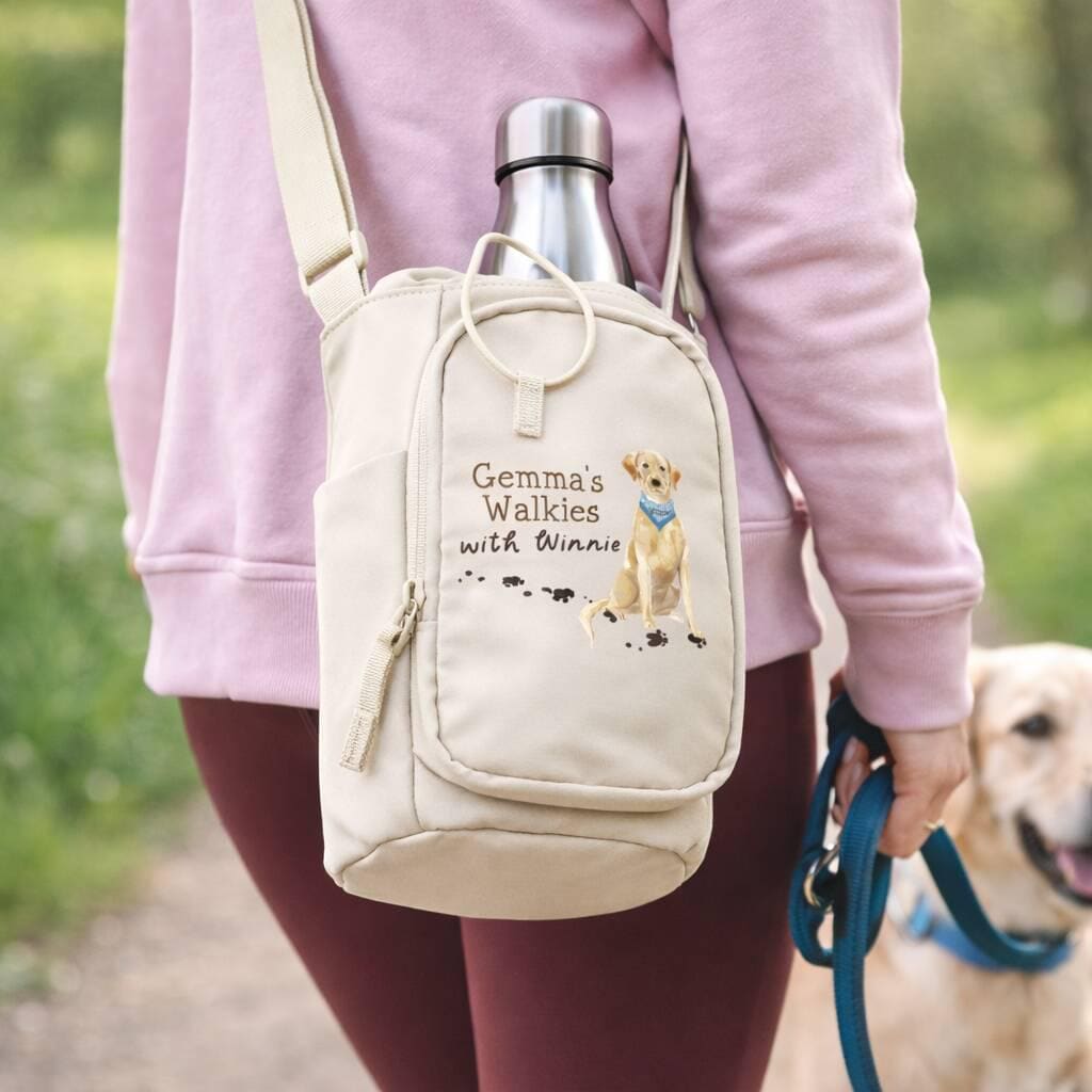 Person holding a beige backpack with 'Gemma's Walkies with Winnie' text and a dog on a leash.