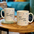 Two mugs with 'Best Grandma Ever!' and 'Best Nanny Ever!' text on a wooden table.