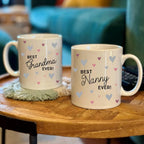 Two mugs with 'Best Grandma Ever!' and 'Best Nanny Ever!' text on a wooden table.
