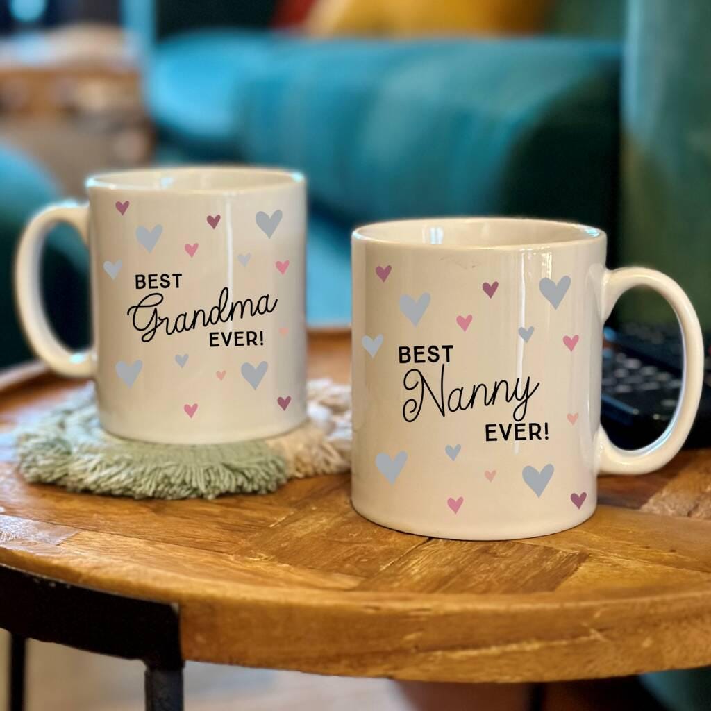 Two mugs with 'Best Grandma Ever!' and 'Best Nanny Ever!' text on a wooden table.