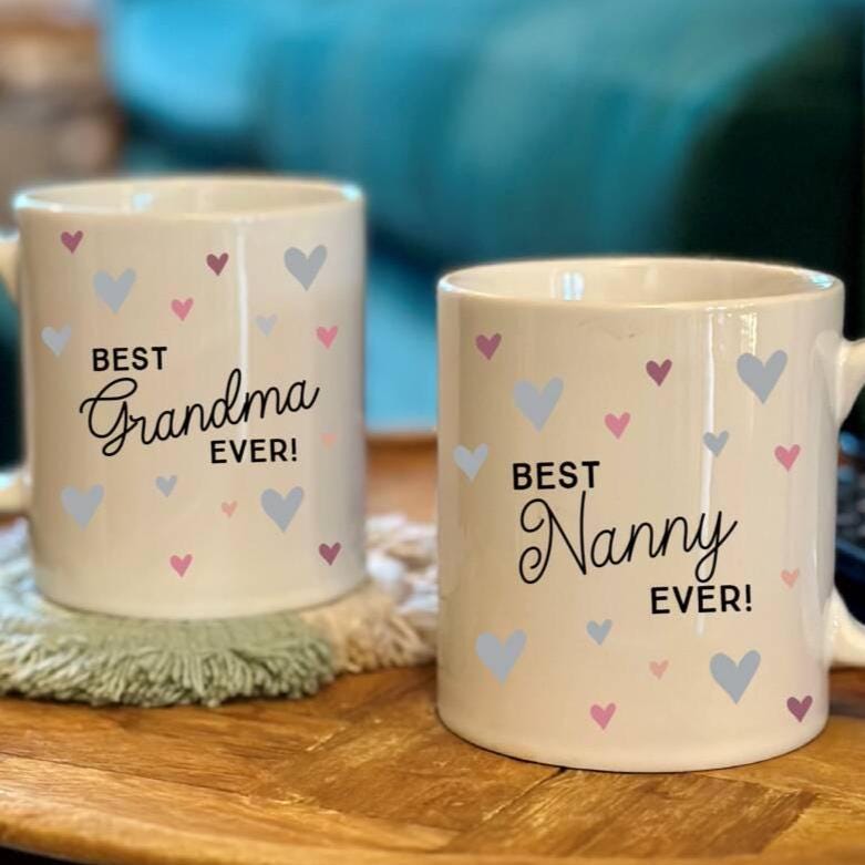 Two mugs with 'Best Grandma Ever!' and 'Best Nanny Ever!' text on a wooden surface.