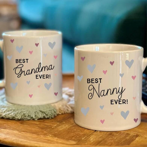 Two mugs with 'Best Grandma Ever!' and 'Best Nanny Ever!' text on a wooden surface.