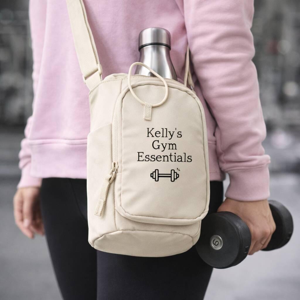 Person holding a beige backpack labeled 'Kelly's Gym Essentials' with a water bottle and dumbbell.