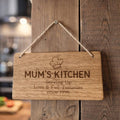Wooden sign with 'Mum's Kitchen' engraving hanging on a wooden wall.