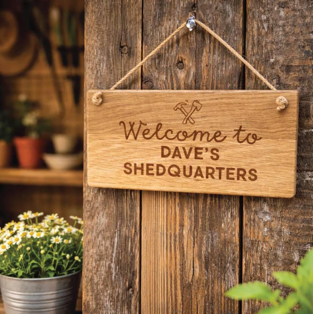 Wooden sign with 'Welcome to Dave's Shedquarters' text hanging on a wooden wall.