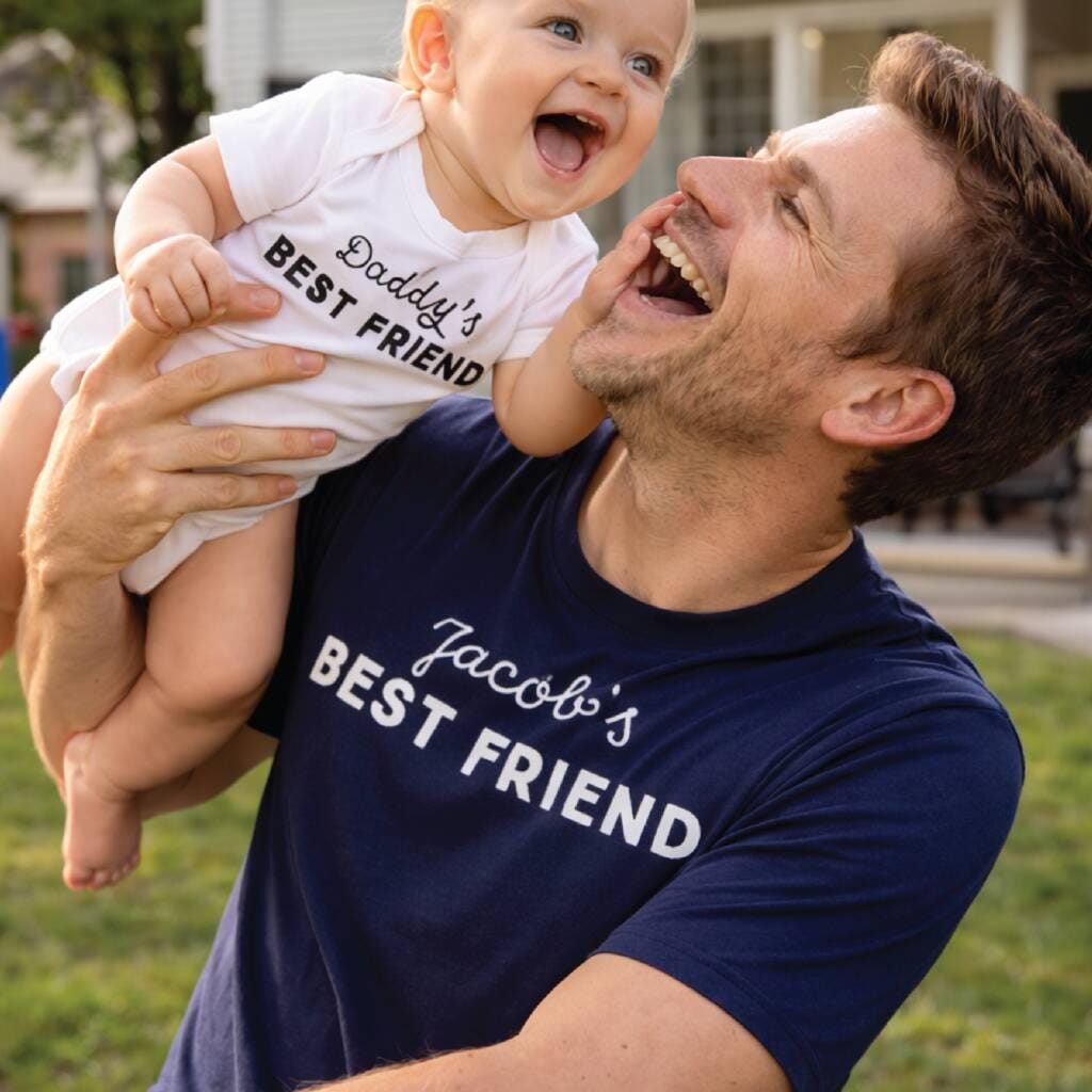 Man holding a baby both wearing shirts with text in an outdoor setting