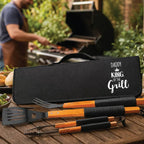 Black BBQ tool set with wooden handles on a wooden table, featuring 'Daddy King of the Grill' text.