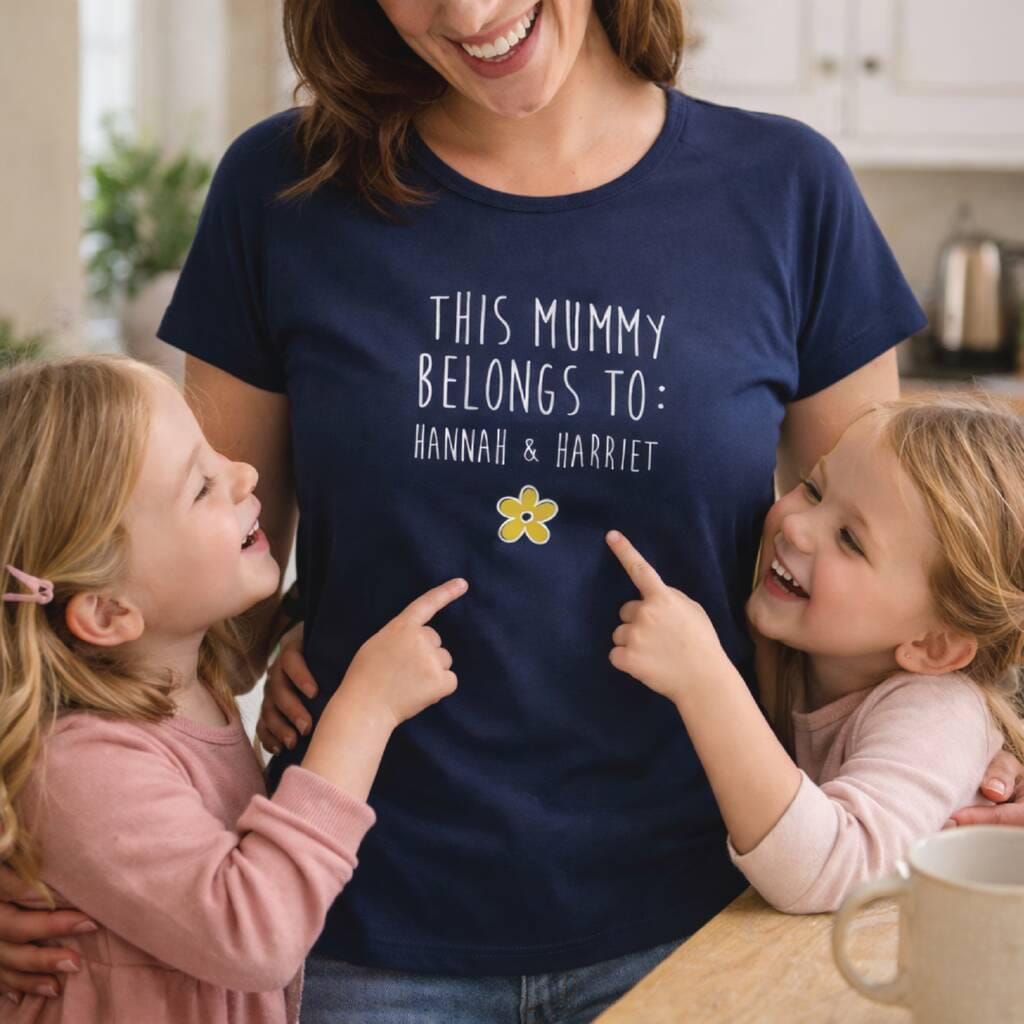 Woman wearing a navy blue t-shirt with 'This Mummy Belongs To: Hannah & Harriet' text and two children pointing at it.