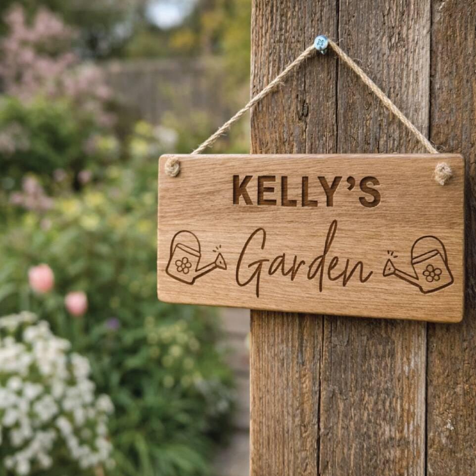Wooden sign with 'KELLY'S Garden' engraved, hanging on a wooden post with garden in the background