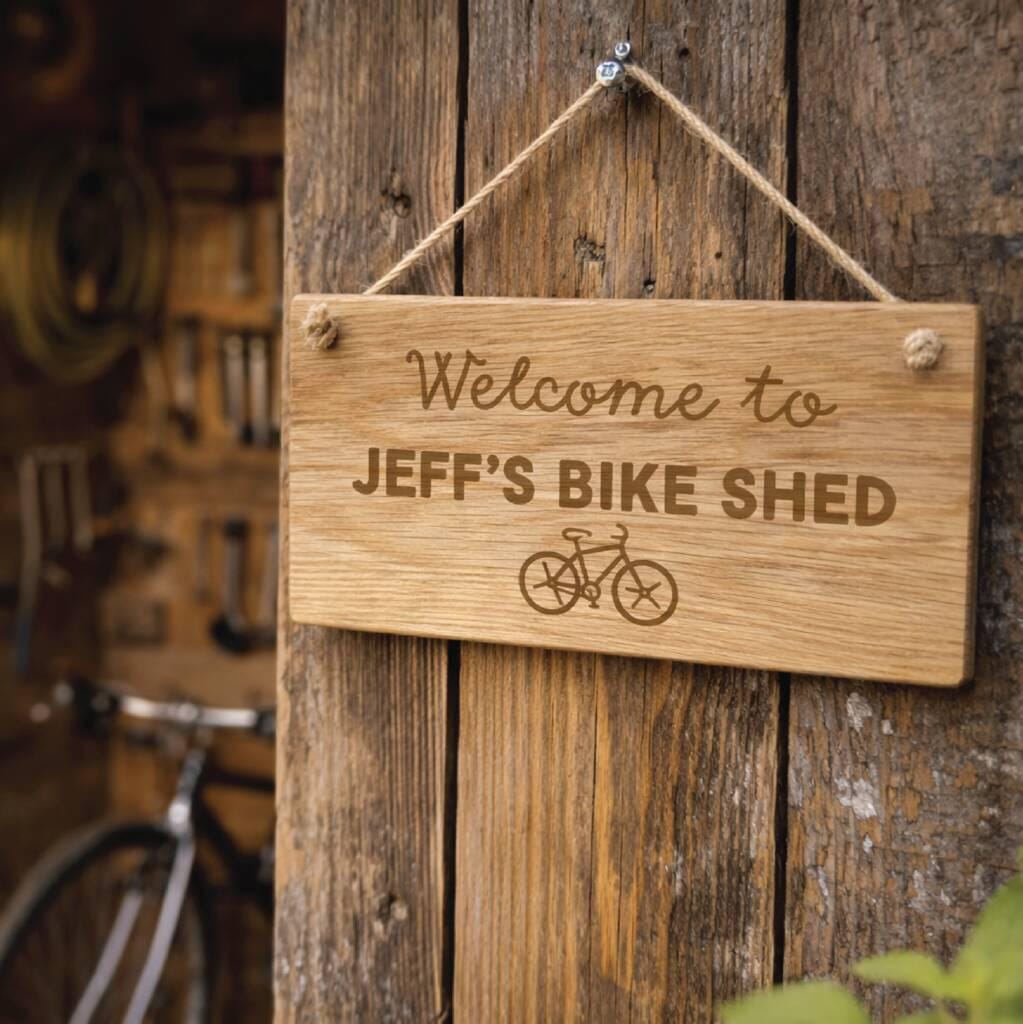 Wooden sign with 'Welcome to JEFF'S BIKE SHED' text and bicycle icon on a wooden background.