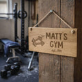Wooden sign with 'Matt's Gym' and dumbbell icon hanging on a wooden door in a gym setting.
