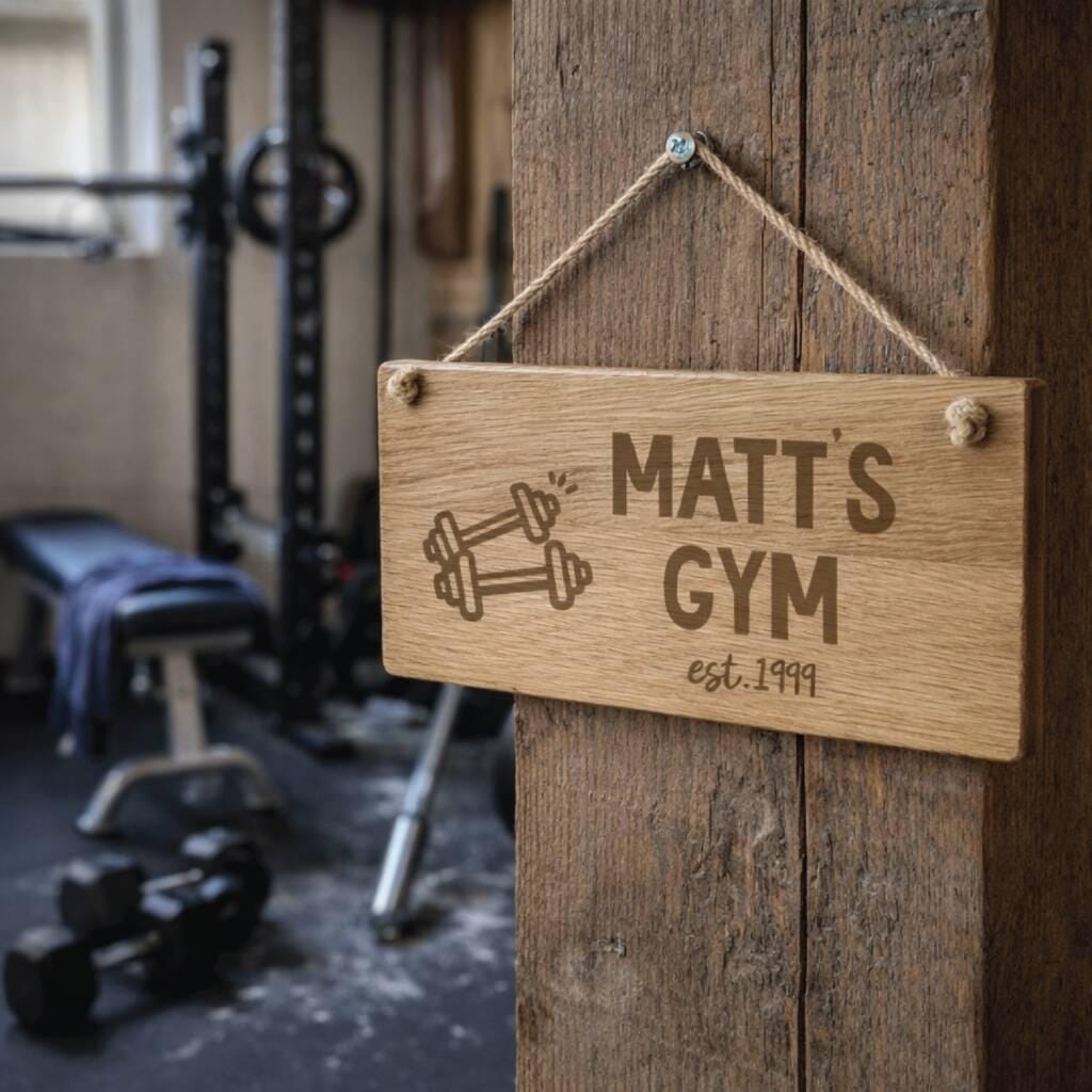 Wooden sign with 'Matt's Gym' and dumbbell icon hanging on a wooden door in a gym setting.