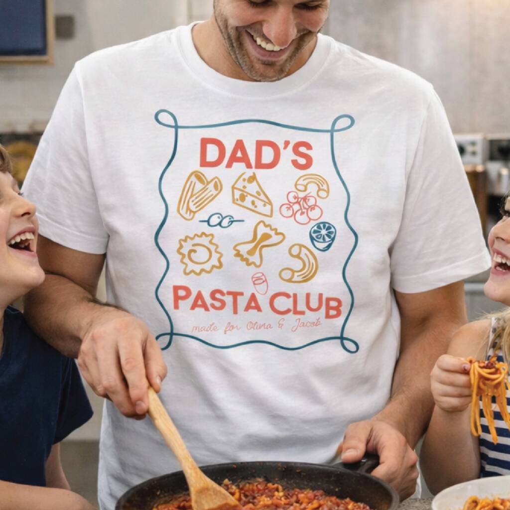Man cooking pasta with children in a kitchen wearing a 'Dad's Pasta Club' t-shirt.