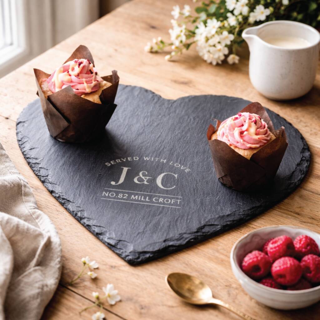 Heart-shaped slate board with 'J&C' initials, cupcakes, and berries on a wooden table.