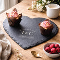 Heart-shaped slate board with 'J&C' initials, cupcakes, and berries on a wooden table.