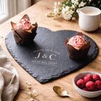 Heart-shaped slate board with 'J&C' initials, cupcakes, and berries on a wooden table.