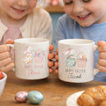 Two children holding personalized Easter mugs with names and illustrations.